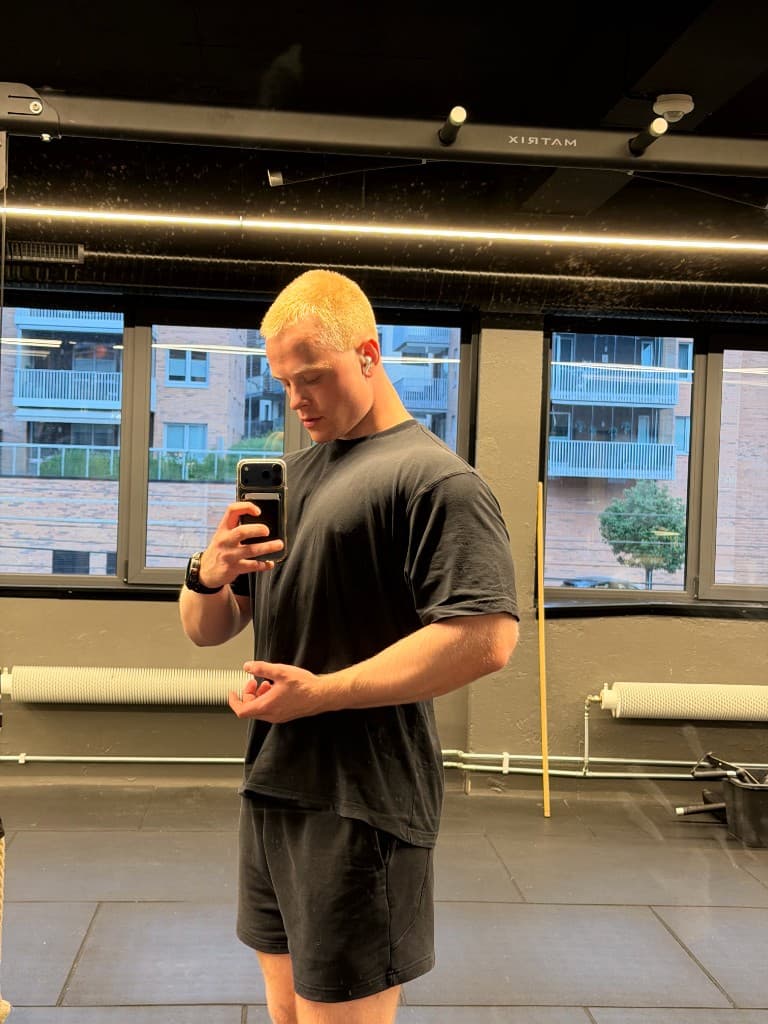 Trygve på gymmen, i svart t-skjorte, ser ned på telefonen.